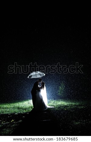 Bride and groom in the night rain hiding under umbrella. Dramatic moment.