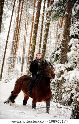 Young attractive man riding black horse at white winter forest.