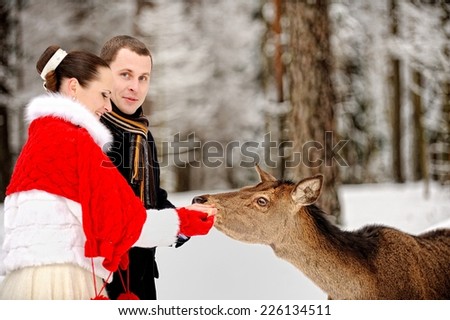 Young elegant couple next to deer in winter forest.