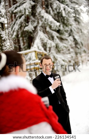 Young elegant man holding wineglass and looking at beautiful elegant woman. Winter forest background.