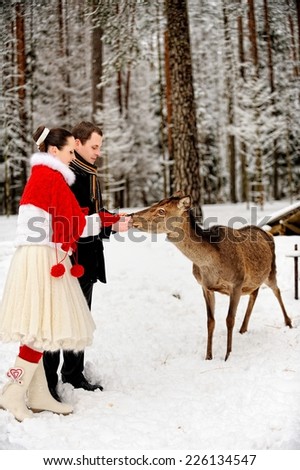Young elegant couple next to deer in winter forest.