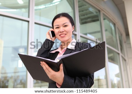 A pretty Chinese business woman smiling outside office building on phone