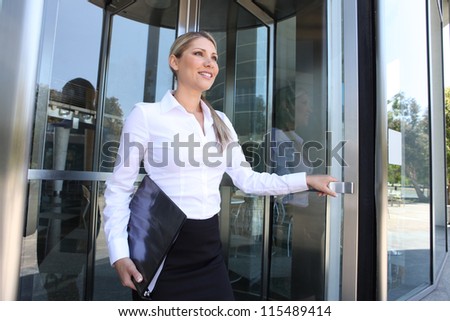 A pretty blonde business woman leaving the office building through glass doors