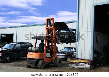 A photo of a man in a forklift carrying a junked car