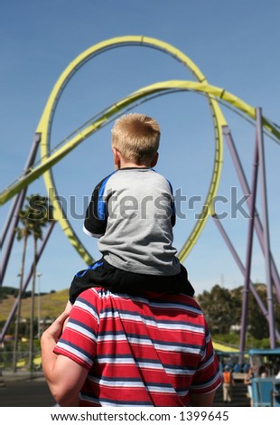 A boy on his fathers back going to ride the roller coaster