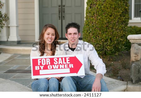 A young couple selling their home holding a sale sign