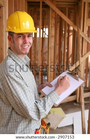 A handsome construction worker with a clipboard at a home building site