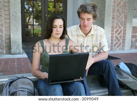 Two students working on the laptop computer in front of the school