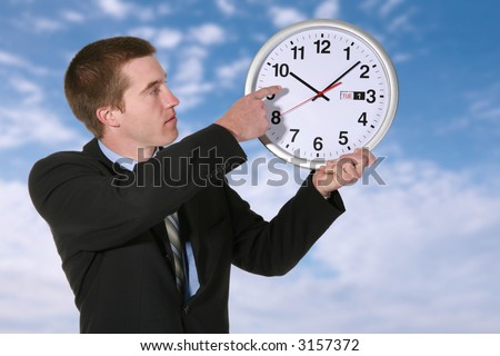 A handsome business man pointing to a clock under a cloudy sky