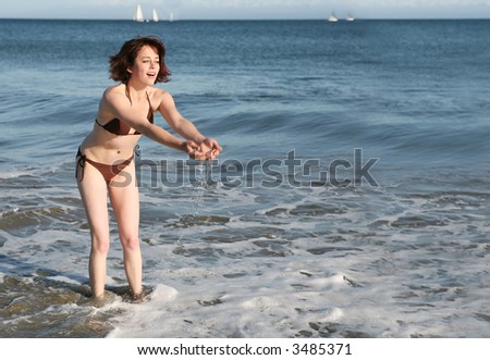 A pretty woman at the beach playing in the water (focus on face, motion blur on hands)
