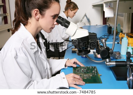 A pretty, young computer technician examining a printed circuit board with a microscope