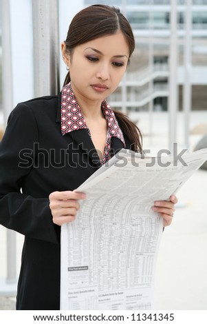 A pretty asian business woman reading the newspaper outside company