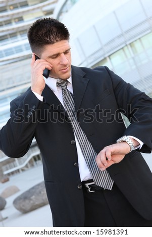 A handsome business man looking at watch and talking on cell phone