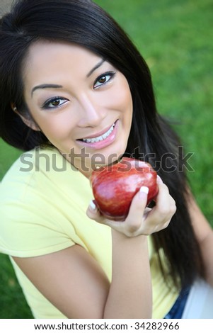 A pretty asian woman eating an apple in the park