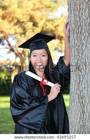 Pretty Asian woman wearing cap and gown holding diploma at graduation
