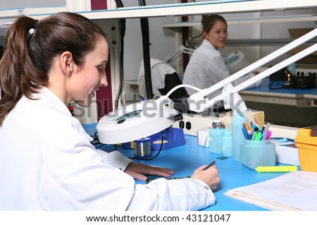 A pretty woman computer technician examining a printed circuit board with a microscope
