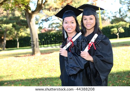 Pretty Asian woman wearing cap and gown holding diploma at graduation