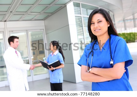 A pretty ethnic nurse outside hospital with team in background