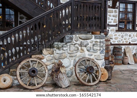Wheels from a cart, old wooden barrels and stones as decoration of an exterior of the house