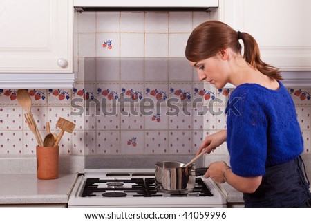 Young woman cooking in the kitchen stirring the contents of the saucepan