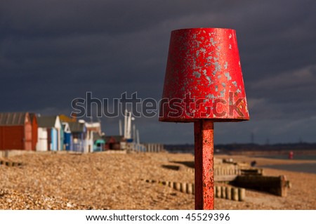 Red marker post on the beach. Differential focus with beach huts out of focus in the background