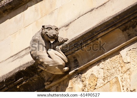 An architectural detail of a stone carving of a grinning cat attached to the wall of a cathedral