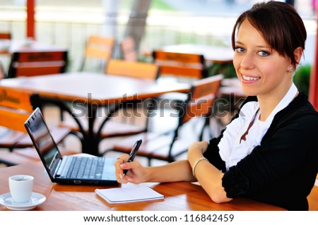 Smiley woman having a cup of coffee and working with laptop and notepad