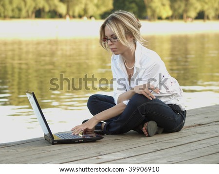 A young businesswoman using a laptop on a wooden river embankment.