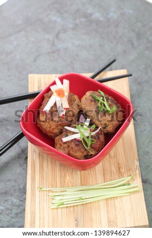 Asian meatballs served in a small red bowl with condiments and chopsticks.