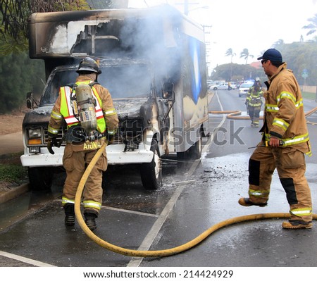 MAUI, HAWAII-April 12: Two firemen actively battling an automotive fire on a city street. Cause of the blaze is unknown, on April 12, 2013. For editorial use.