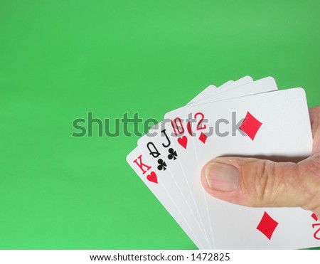 Hand holding five playing cards, on green felt table.