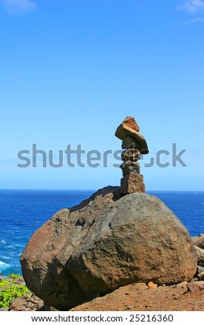Stack of spirit stones on a Hawaiian cliff against the blue sky and ocean
