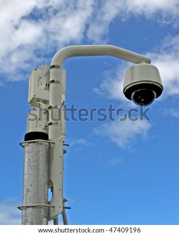 Remote surveillance video camera on a post against the sky
