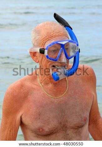 Older man on a beach wearing blue snorkel and dive mask