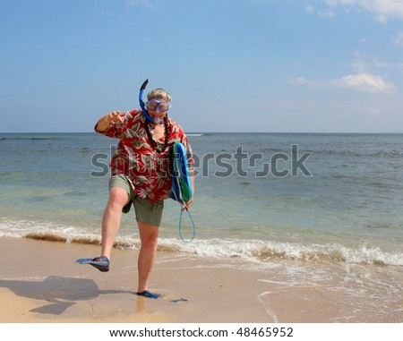 Happy tourist on a tropical beach with snorkel gear, swimfins, surfboard and a floral shirt