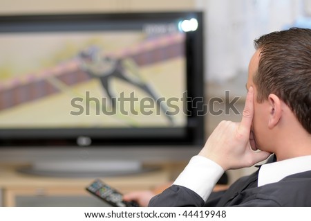 Details of a young man sitting in front of TV and holding a remote control.