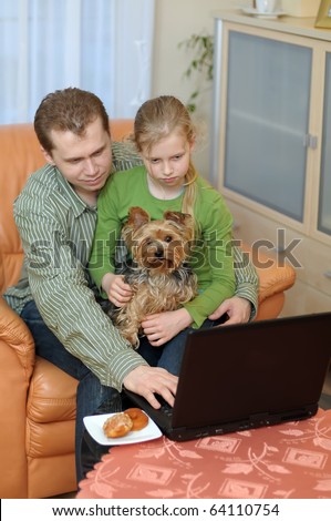 Father and teenage daughter with small dog looking into a portable computer at home.