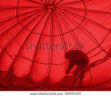 A crew member is silhouetted in red during the inflation process of a hot air balloon.