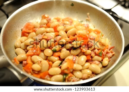 The making of a dish of beans with bacon and tomatos
