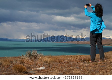 EL CALAFATE, ARGENTINA - DECEMBER 27, 2013 : Tourist woman pictures Lago Argentino. The lake lies within the Los Glaciares National Park and is the biggest freshwater lake in Argentina