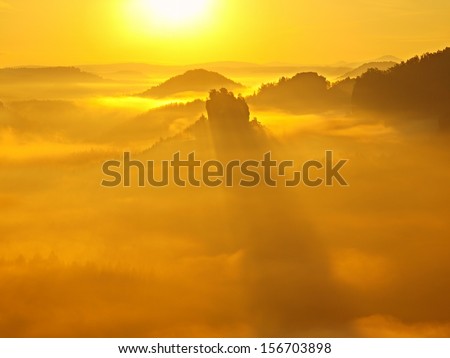 Golden sunrise in a beautiful mountain of Saxony Switzerland. Sandstone peaks increased from gold foggy background, the fog is yellow-orange gold due to first strong sun rays.