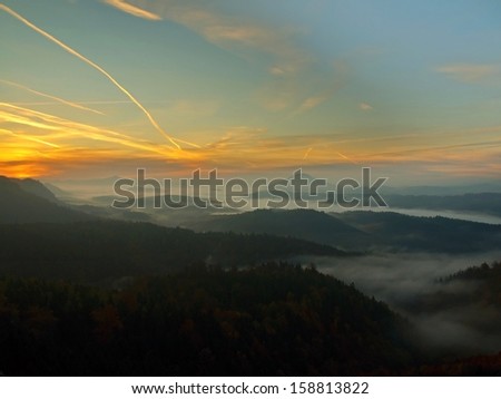 Sunrise in a beautiful mountain of Czech-Saxony Switzerland. Sandstone peaks and hills increased from foggy background, the fog is orange due to sun rays.