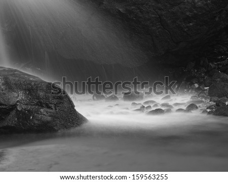 Water spray below small waterfall on mountain stream, water is falling over mossy sandstone boulder. The spray create on level and gravel milky water.