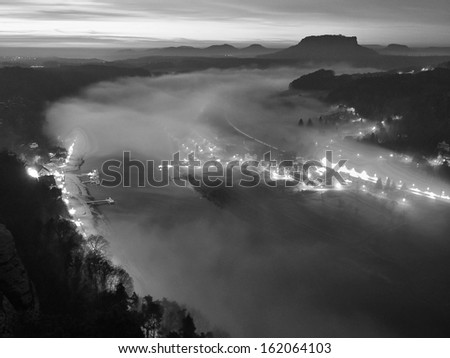 Early morning above river after rainy night, fog is shaking above water level and river banks. Autumn landscape, daybreak at horizon. Traffic lights are shining in the mist. Black and white photo.