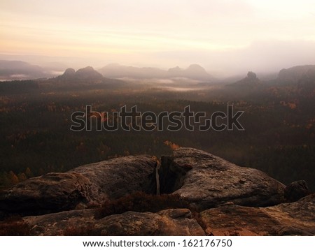 Pink daybreak in a beautiful mountain of Saxony Switzerland. Sandstone peaks and hills increased from pink foggy background, the fog is pink-orange due to first sun rays.