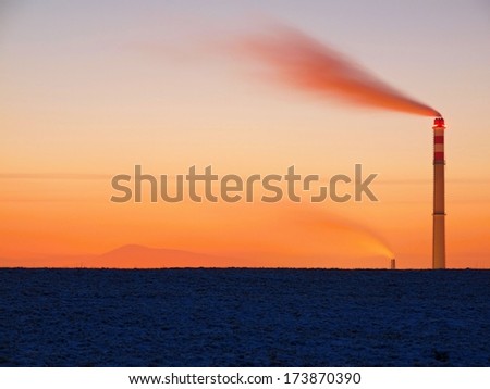 Smoking chimney after sunset of winter day, red sky and dark ground with first powder snow.