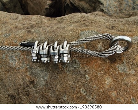 Iron twisted rope fixed in block by screws snap hooks. Detail of rope end anchored into sandstone rock