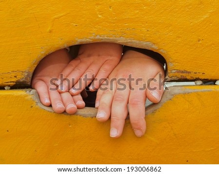 Tree children hands with small fingers through hole in orange wooden climbing wall ladder on kids playground