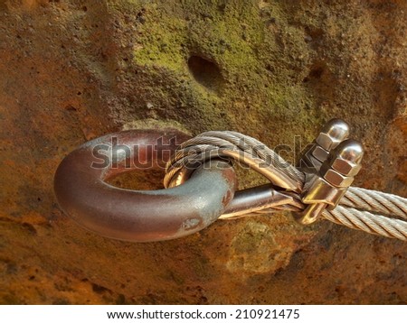 Detail of rope end anchored into sandstone rock. Iron twisted rope fixed in steel hanger by screws snap hooks.