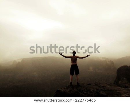 Climber in black pants. Gesture of triumph. Naked tourist on the peak of sandstone rock in national park Saxony Switzerland watching into misty landscape.